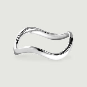 A polished silver ring with a curved band rests on a light gray surface.