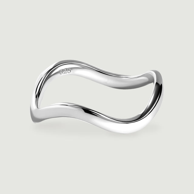 A polished silver ring with a curved band rests on a light gray surface.