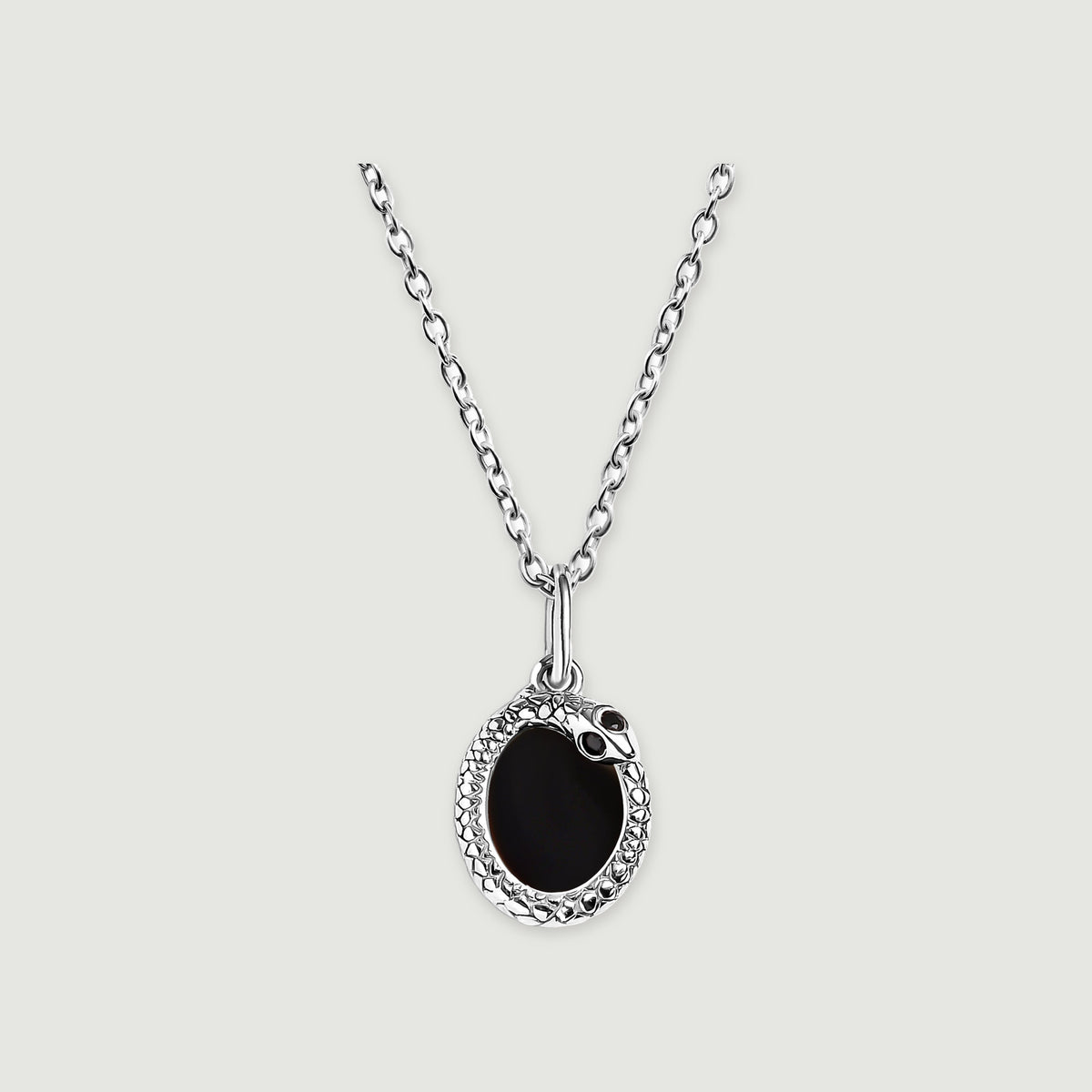 A silver-tone necklace displays a black oval pendant with a textured rim against a pale gray surface.