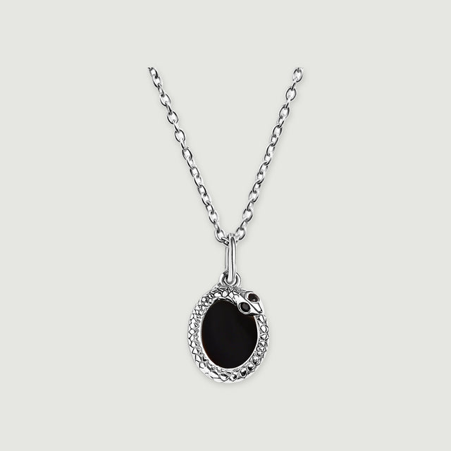 A silver-tone necklace displays a black oval pendant with a textured rim against a pale gray surface.