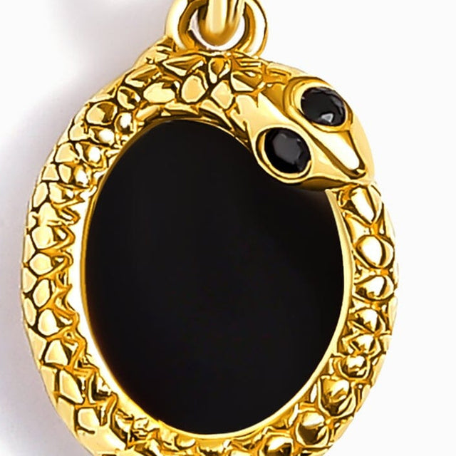 A close view shows the glossy black stone, two small dark accents, and textured yellow gold setting.