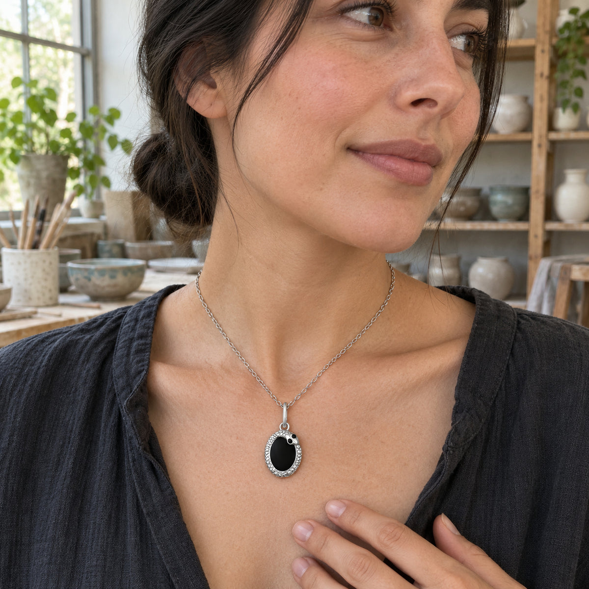 A silver-tone black-stone necklace is worn with a charcoal shirt in a pottery studio.