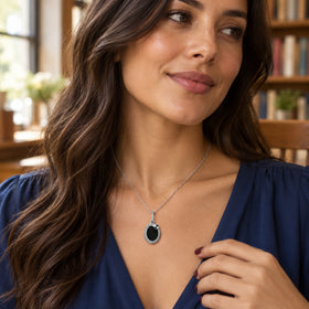 A woman in a blue blouse wears the silver-tone pendant with bookshelves behind her.