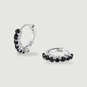 Two silver-colored hoop earrings with round black stones are centered on a light gray surface.
