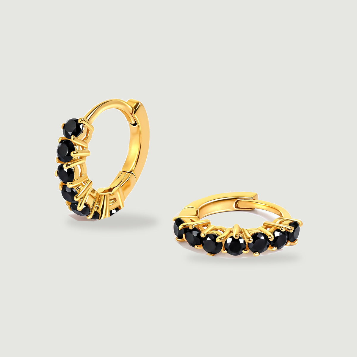 A pair of gold-colored hoops with glossy black stones rests on a pale gray background.