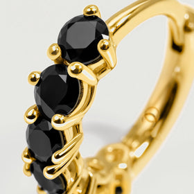 Round black gemstone facets and polished gold-colored claws fill the close-up view.
