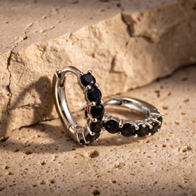 Two silver-colored black-stone hoops lean together on a textured beige stone surface.