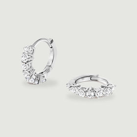 A pair of silver-tone white topaz hoop earrings rests on a light gray surface.