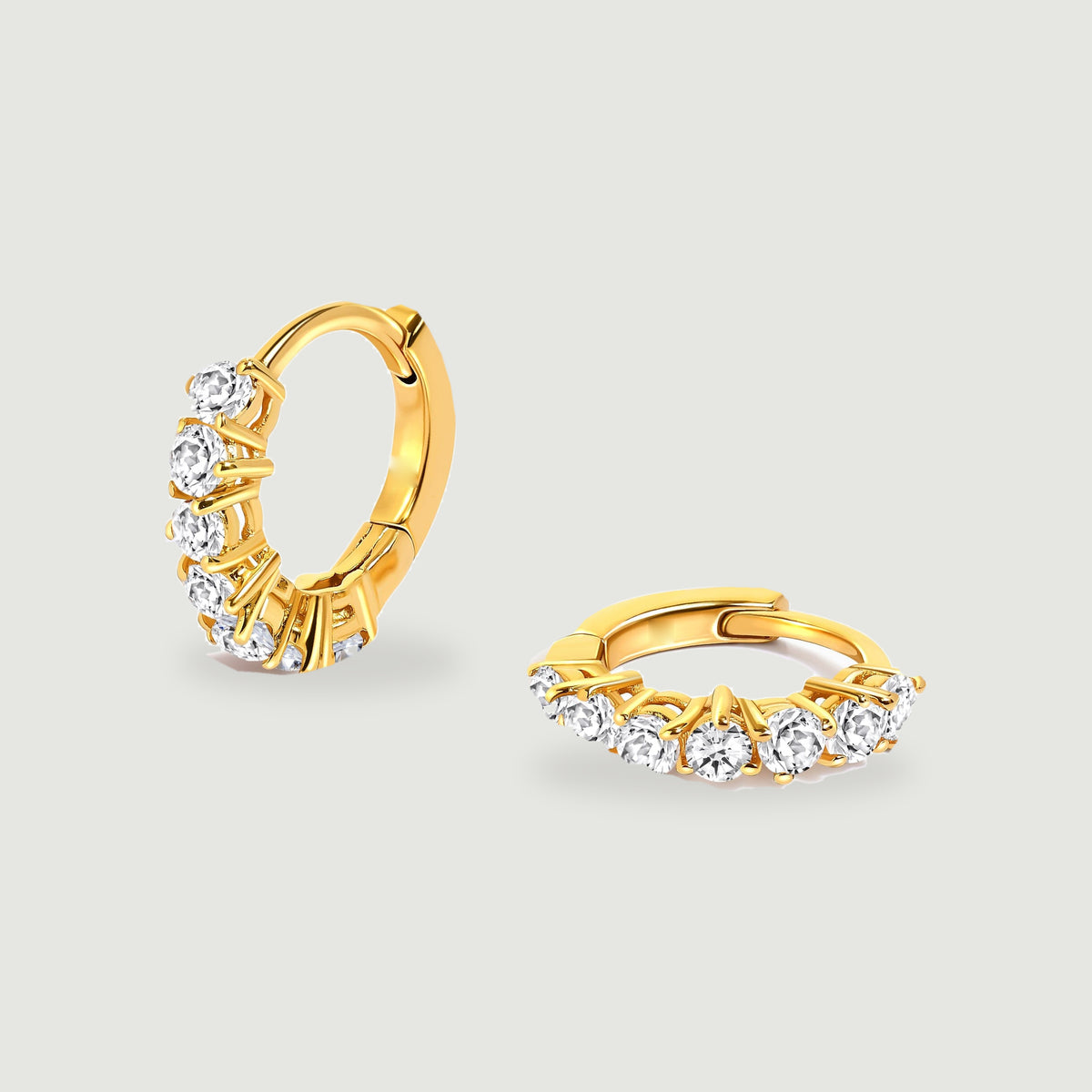 Two yellow gold-tone hoops display clear round stones above soft shadows.