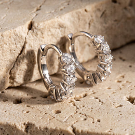Two silver-tone hoops stand on textured stone with their curved backs visible.