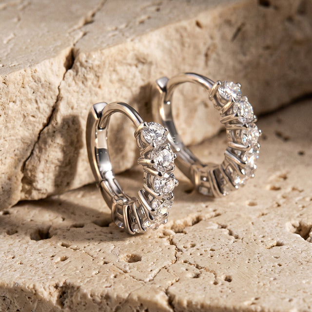 Two silver-tone hoops stand on textured stone with their curved backs visible.