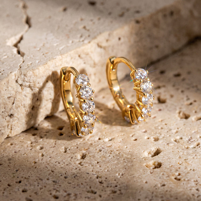Yellow gold-tone white topaz earrings lean against a textured beige stone.