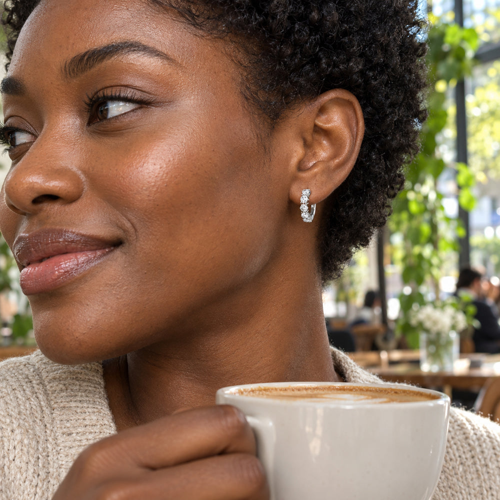 A silver-tone white topaz hoop is worn by a woman with short curls in a bright cafe.