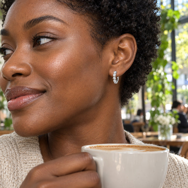 A silver-tone white topaz hoop is worn by a woman with short curls in a bright cafe.