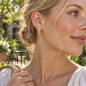 A woman with blonde hair wears a yellow gold-tone white topaz hoop in a sunlit garden.