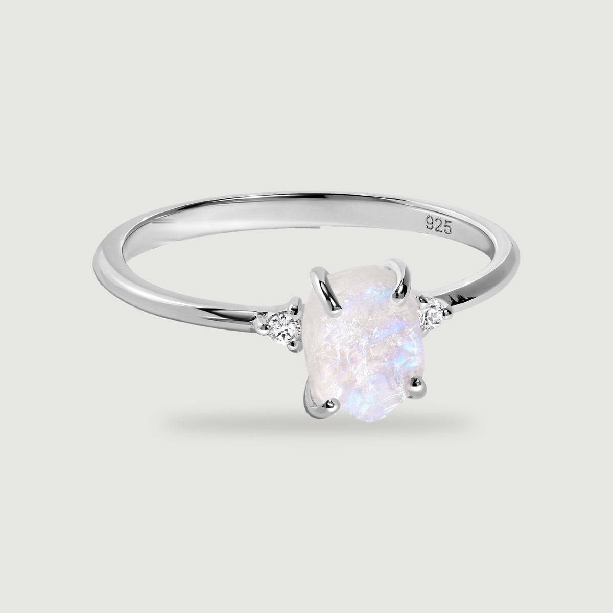 A sterling silver ring holds a rough pale moonstone between two round side stones on a light gray background.