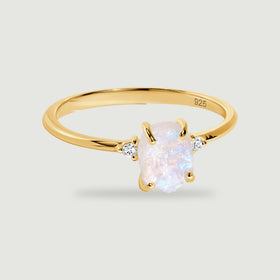 A yellow gold vermeil ring with a pale rough center stone and two small clear stones rests above a soft shadow.