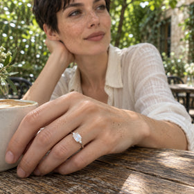 A woman with short dark hair wears the silver moonstone ring beside a coffee cup at an outdoor wooden table.