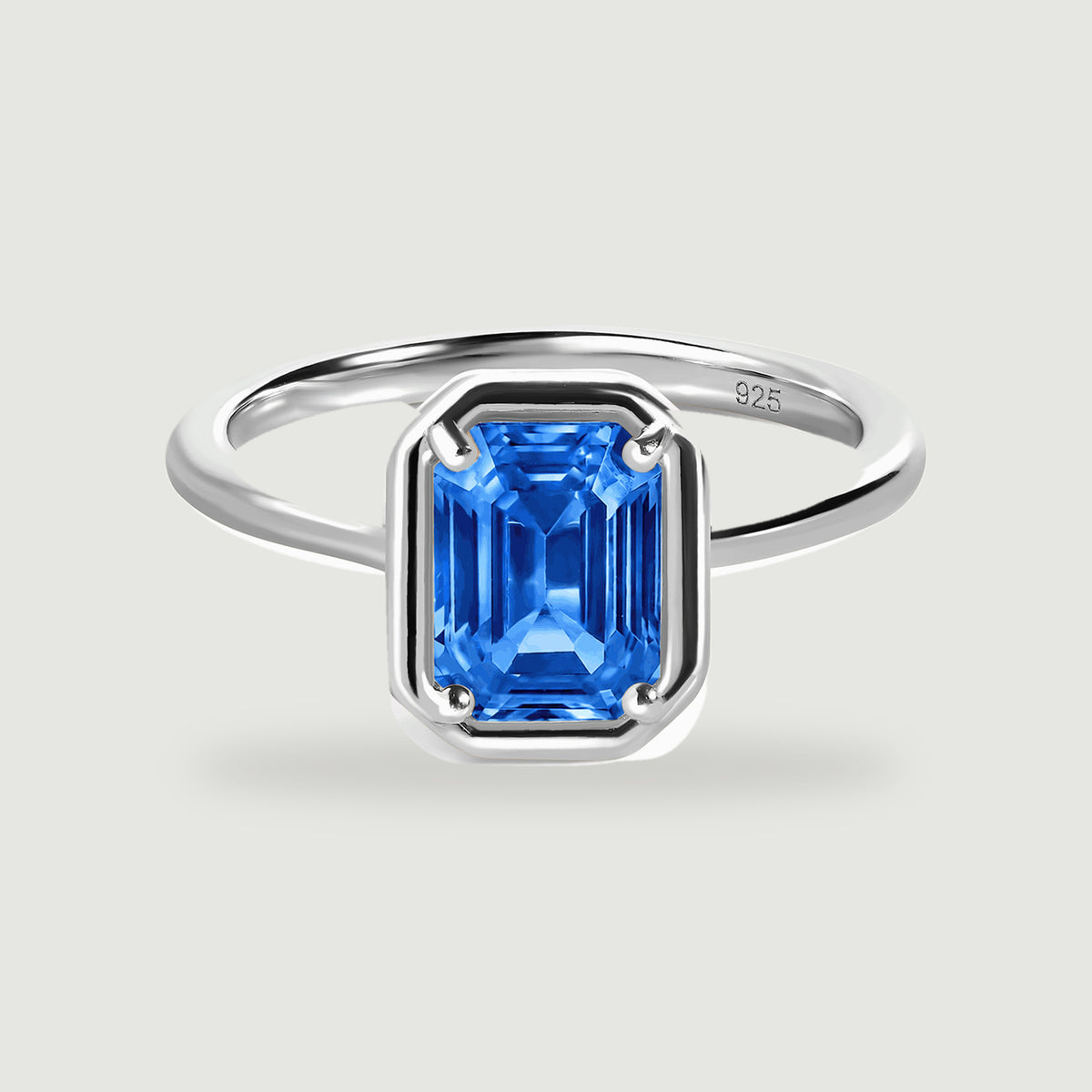 A polished silver ring with a rectangular blue gemstone stands on a light gray background.