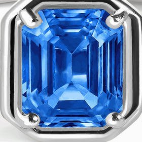 Four silver prongs surround the stepped facets of a rectangular bright blue gemstone.