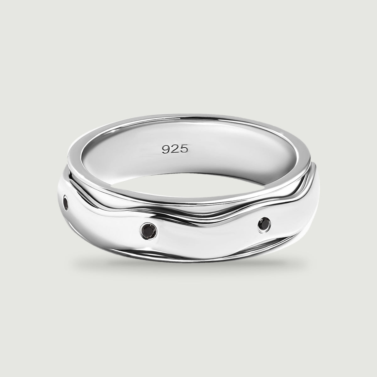 A polished silver ring with small round black stones and a wavy outer band sits on a light gray surface.