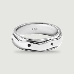 A polished silver ring with small round black stones and a wavy outer band sits on a light gray surface.