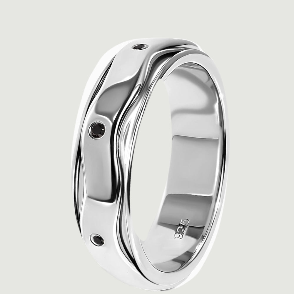 The silver ring stands on its edge, showing the layered wavy band and inset black stones.