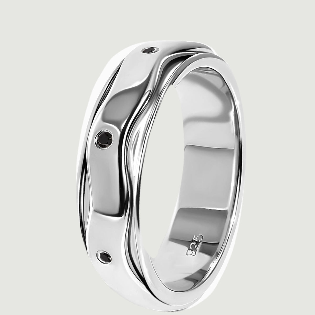 The silver ring stands on its edge, showing the layered wavy band and inset black stones.