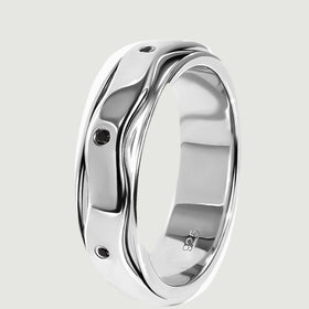 The silver ring stands on its edge, showing the layered wavy band and inset black stones.