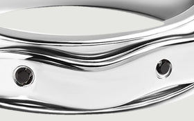 A close view shows round black stones set into the broad reflective silver band.