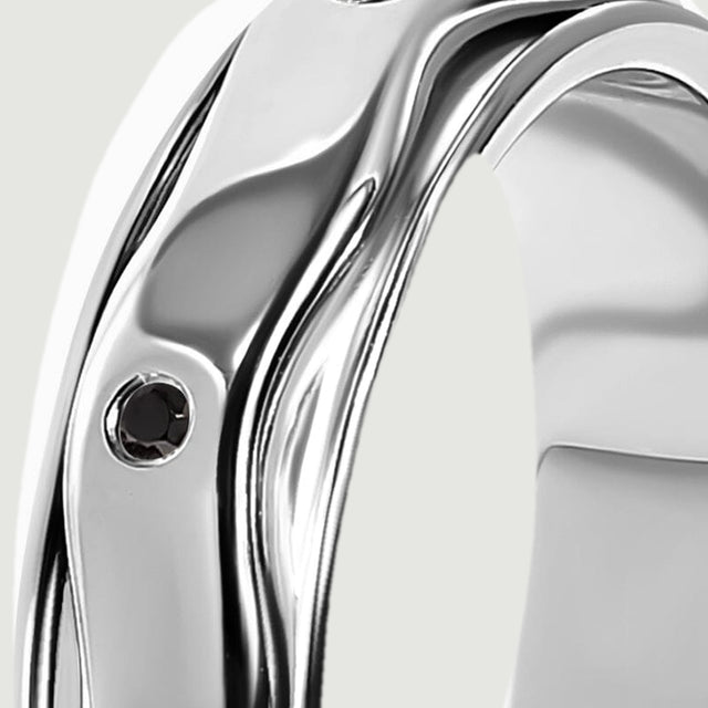 Polished silver rails follow the curved edge of the ring beside a small black stone.
