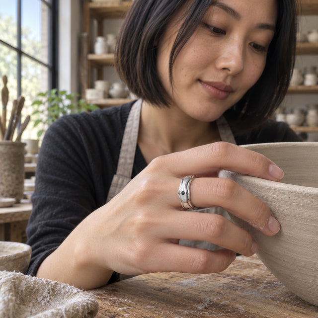 A woman with a short dark bob wears the silver ring while holding a stoneware bowl in a pottery workshop.