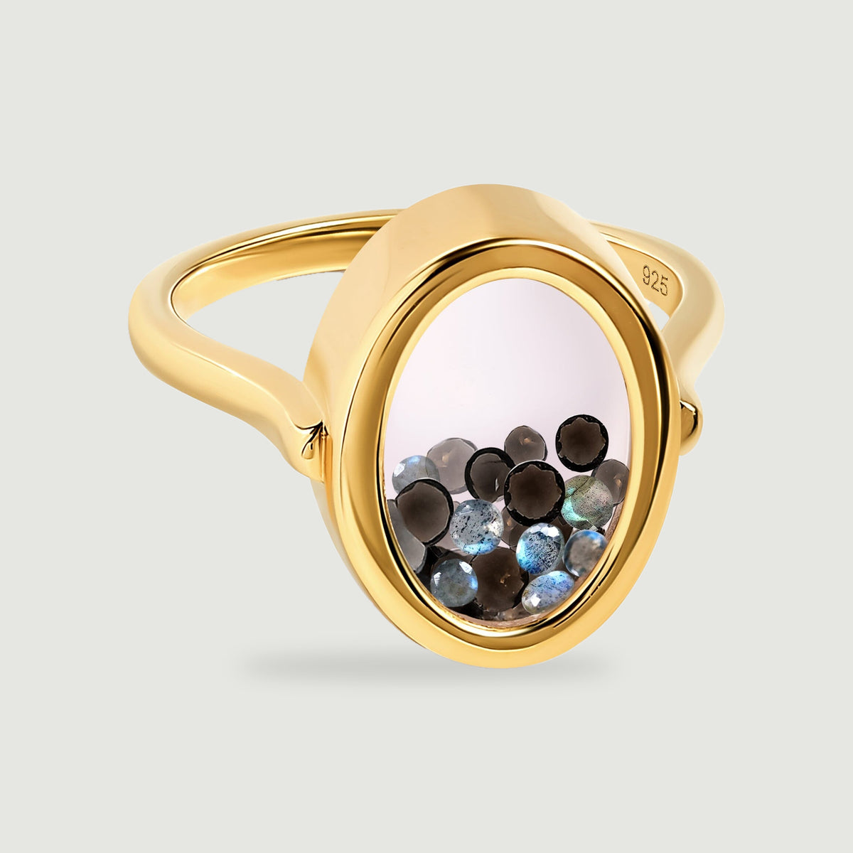 A yellow gold vermeil ring with a clear oval window contains small dark and iridescent gems against a pale gray background.
