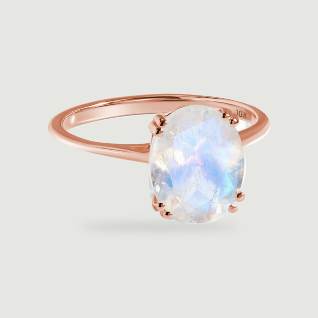 A rose gold solitaire ring displays a pale oval moonstone and rounded paired prongs.