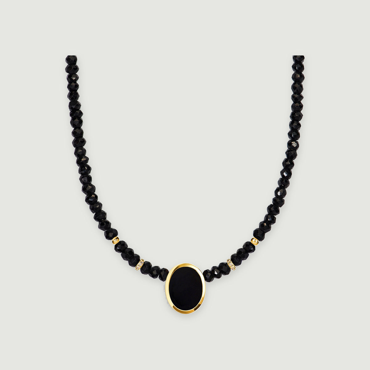A black faceted bead necklace with an oval black pendant and yellow gold bezel is centered on a light gray background.