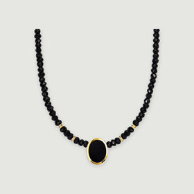 A black faceted bead necklace with an oval black pendant and yellow gold bezel is centered on a light gray background.