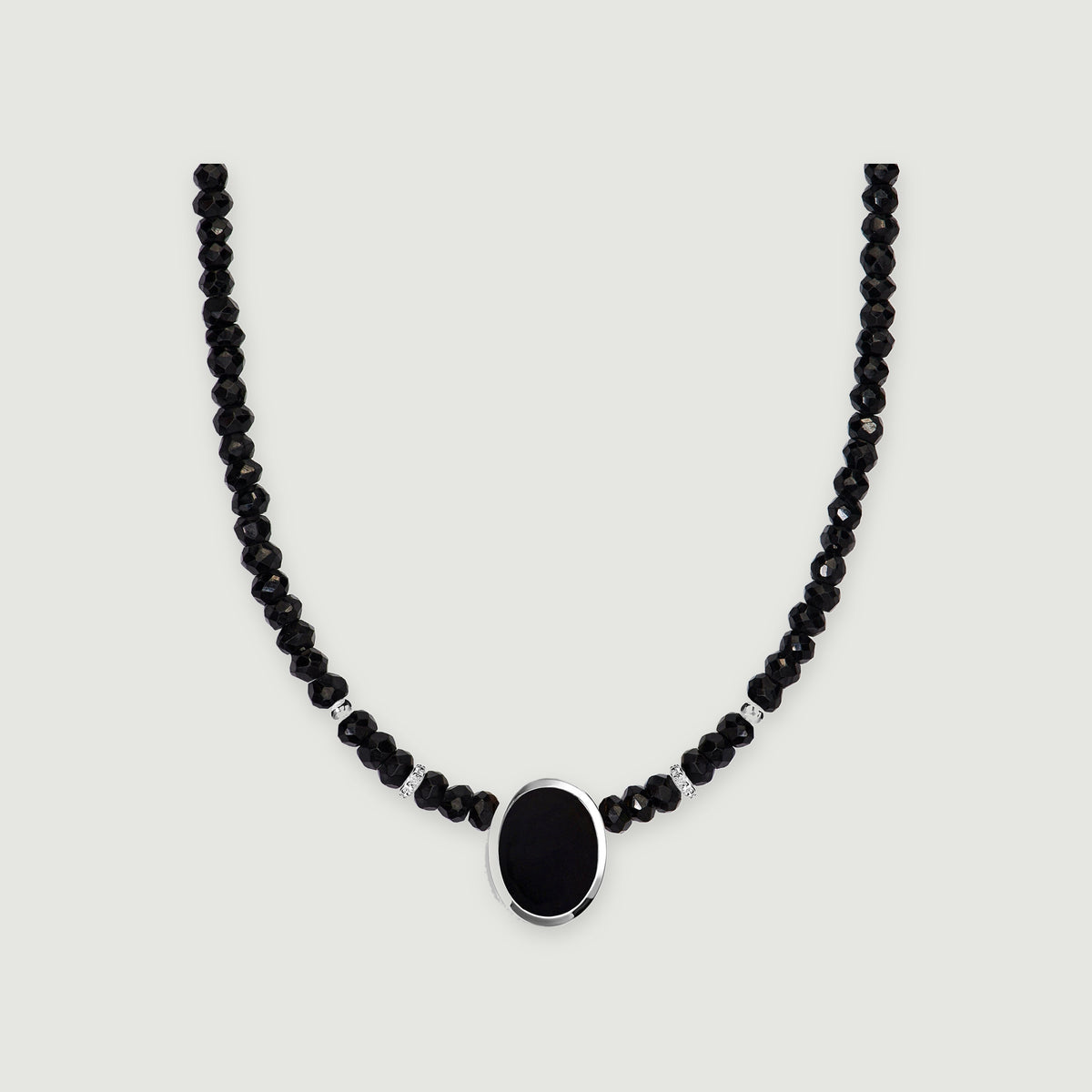 A strand of faceted black beads curves around an oval black pendant in a polished silver setting on light gray.