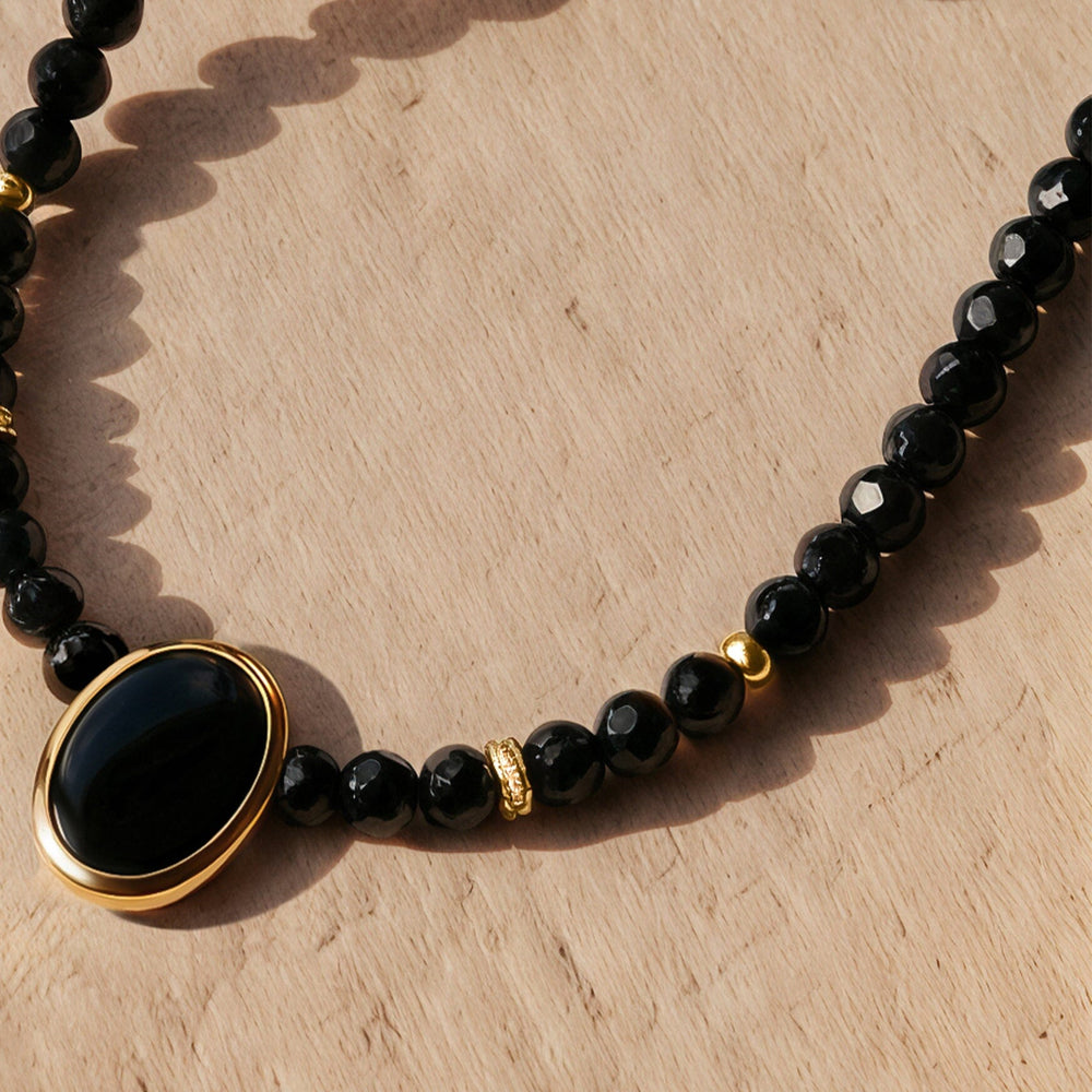Yellow gold accents and a glossy oval black pendant rest with faceted black beads on a pale wooden surface.