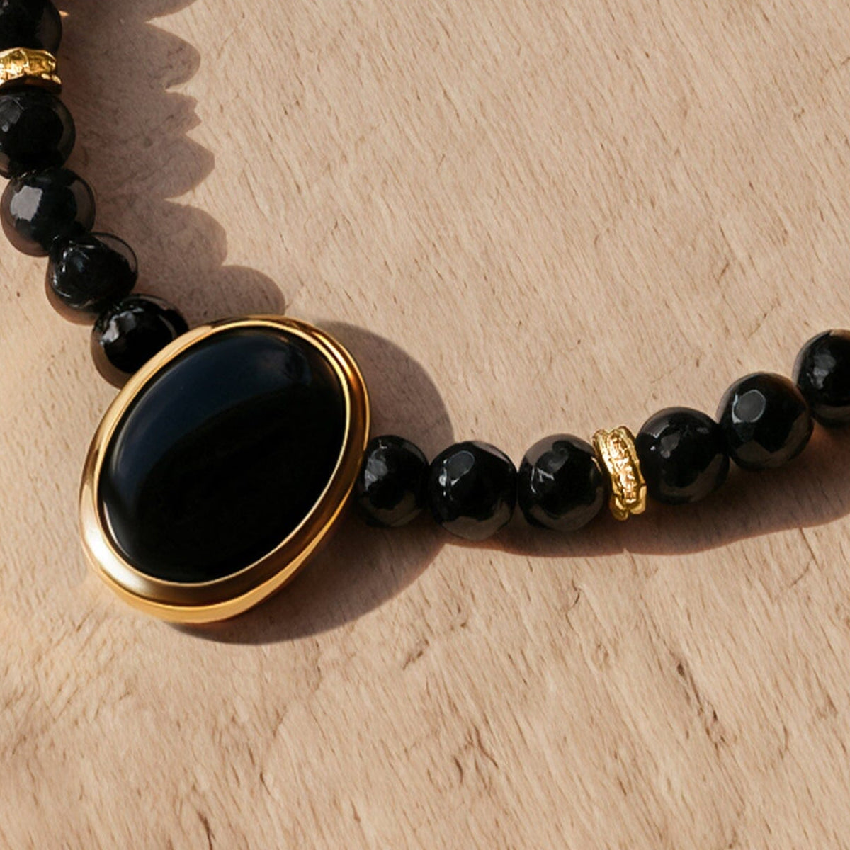 The oval black pendant sits in a yellow gold rim between faceted beads and clear stone set spacers.