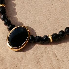 The oval black pendant sits in a yellow gold rim between faceted beads and clear stone set spacers.