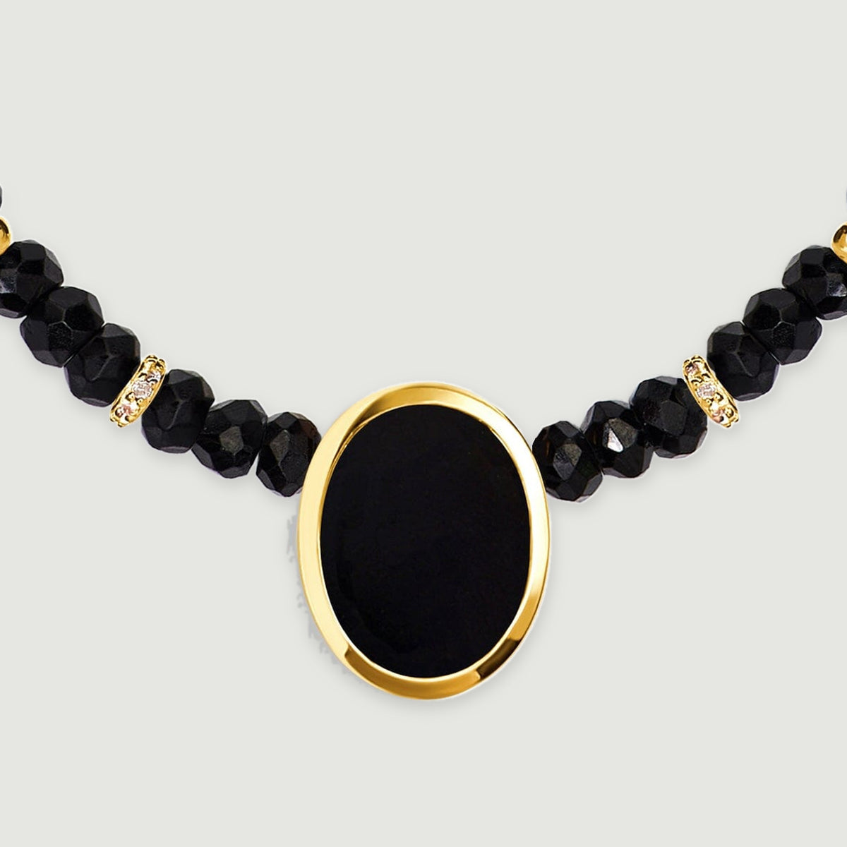 A frontal detail shows a smooth oval black stone inside a yellow gold bezel below two clear stone set spacers.