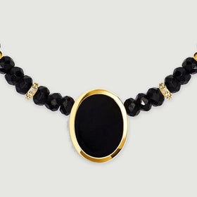 A frontal detail shows a smooth oval black stone inside a yellow gold bezel below two clear stone set spacers.