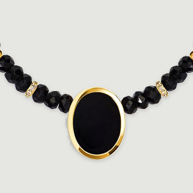 A frontal detail shows a smooth oval black stone inside a yellow gold bezel below two clear stone set spacers.