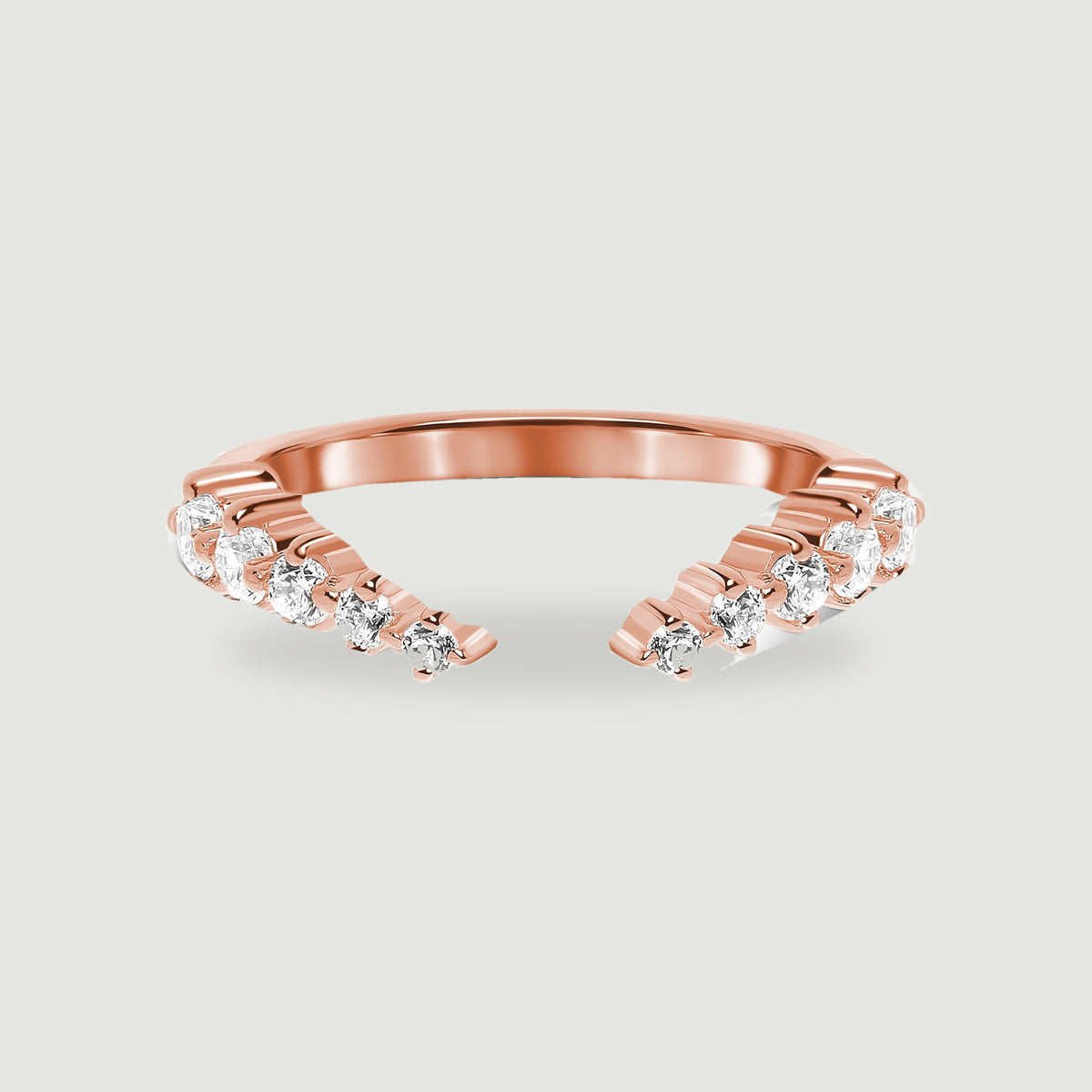 A rose gold vermeil open band is centered on a light gray surface with clear stones facing forward.