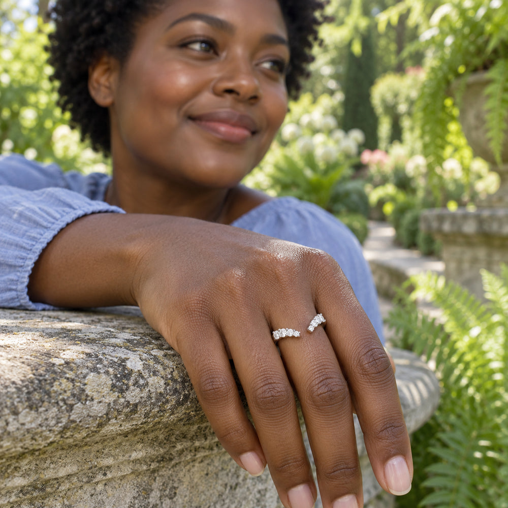 A silver open ring with clear stones is worn on a hand resting on a stone garden railing.
