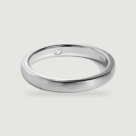 A complete silver ring shows its brushed exterior, polished edges, and a clear round stone inside the band.
