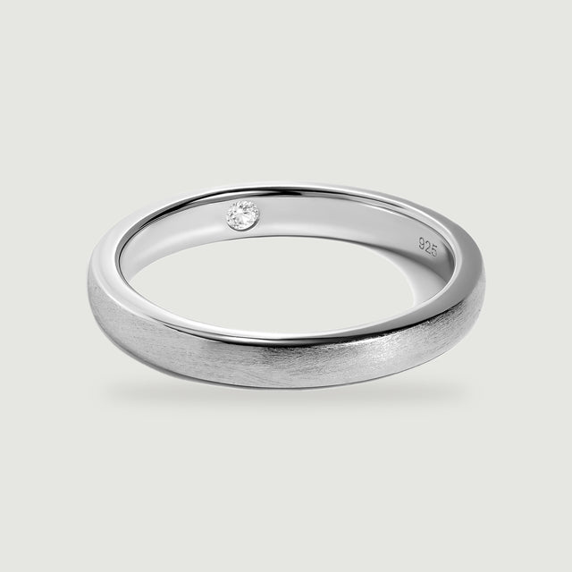 A complete silver ring shows its brushed exterior, polished edges, and a clear round stone inside the band.