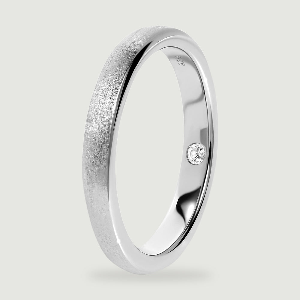 An upright silver ring reveals the smooth inner band, rounded rim, and inset clear stone.