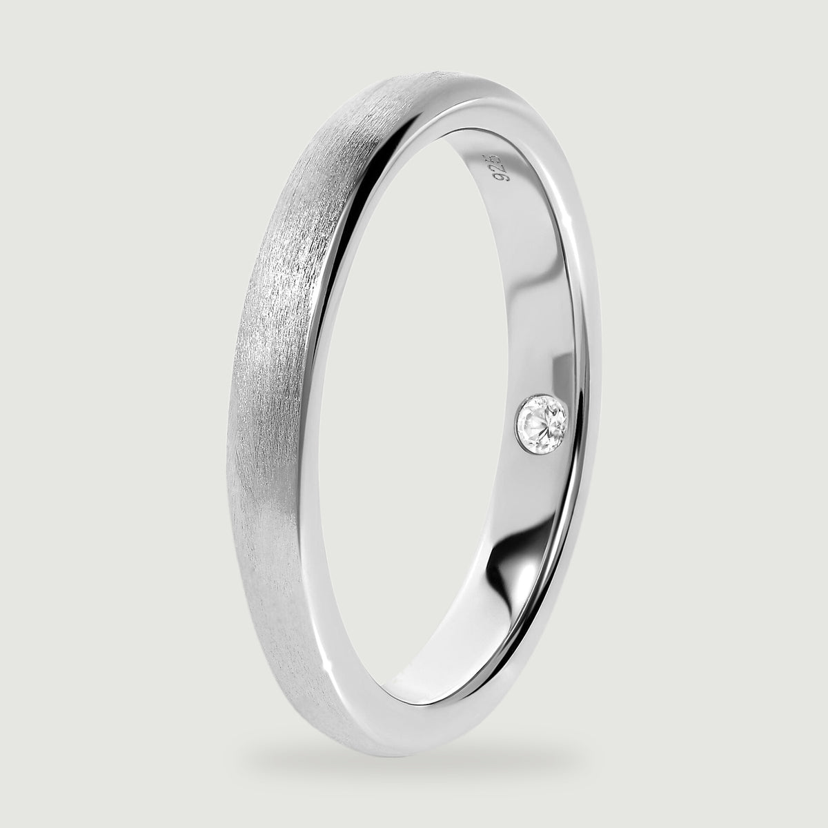 An upright silver ring reveals the smooth inner band, rounded rim, and inset clear stone.