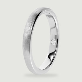 An upright silver ring reveals the smooth inner band, rounded rim, and inset clear stone.